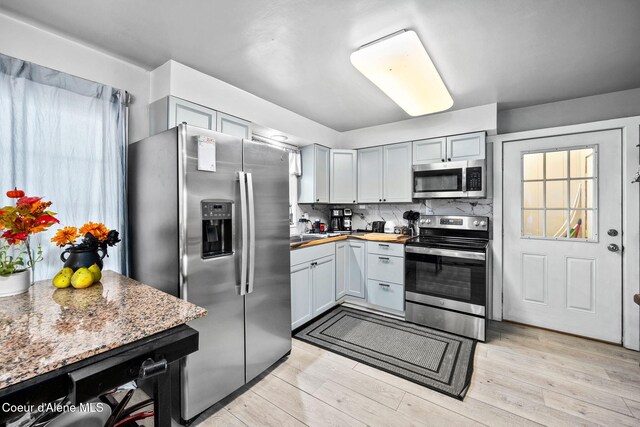 kitchen with light wood-style flooring, backsplash, and stainless steel appliances
