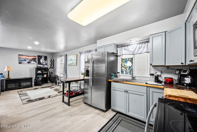 kitchen with light wood finished floors, wooden counters, stainless steel fridge with ice dispenser, a sink, and black electric range oven