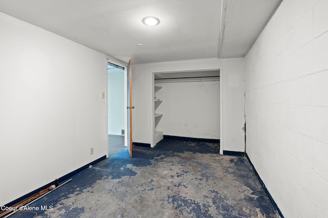 unfurnished bedroom featuring a closet, concrete block wall, concrete floors, and baseboards