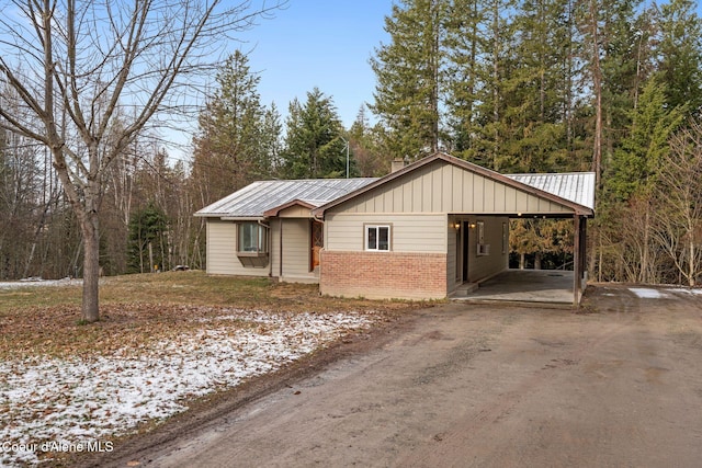 view of front of home with an attached carport, driveway, a chimney, brick siding, and metal roof