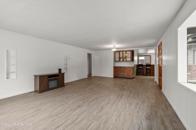 unfurnished living room with built in features, wood finished floors, a textured ceiling, a glass covered fireplace, and a notable chandelier