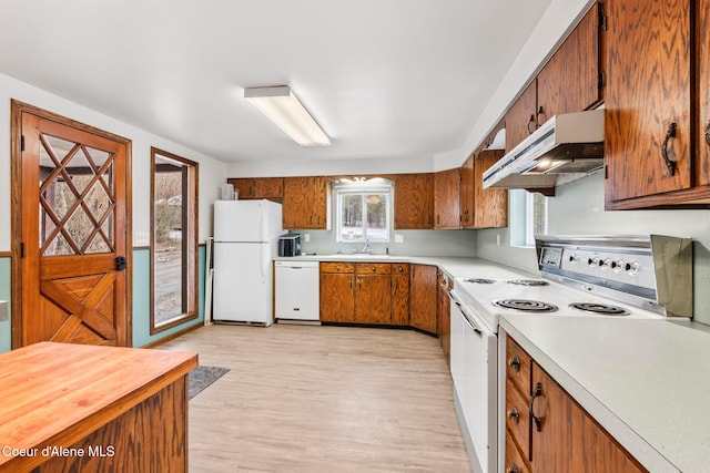 kitchen featuring under cabinet range hood, light wood-type flooring, light countertops, brown cabinets, and white appliances