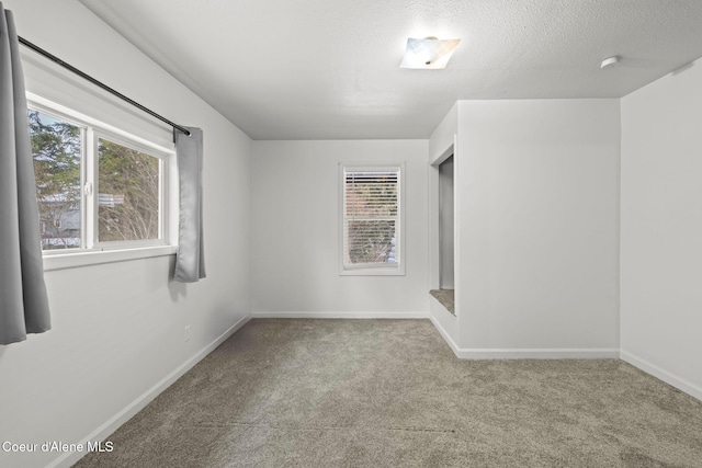 carpeted empty room featuring baseboards, plenty of natural light, and a textured ceiling