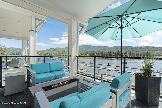 view of patio with a wooded view, a balcony, a water and mountain view, and an outdoor living space with a fire pit