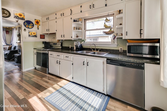 kitchen with open shelves, a wainscoted wall, dark countertops, a sink, and stainless steel appliances