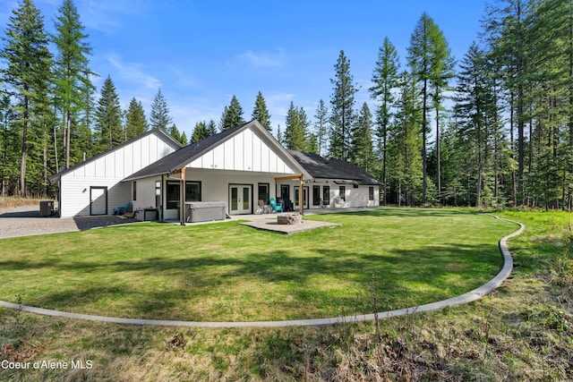 rear view of property featuring board and batten siding, a patio area, a hot tub, a lawn, and french doors