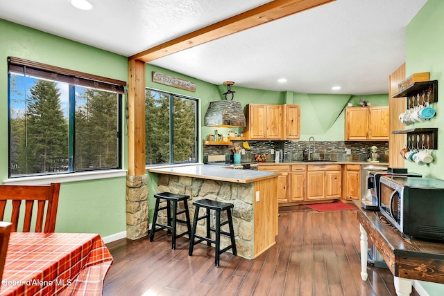 kitchen with a sink, a kitchen bar, decorative backsplash, a peninsula, and dark wood-style flooring