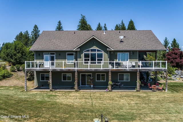 rear view of house featuring a patio area, a lawn, roof with shingles, and a wooden deck