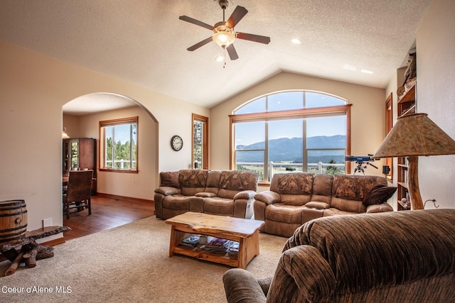 carpeted living room with a ceiling fan, a textured ceiling, a mountain view, arched walkways, and vaulted ceiling