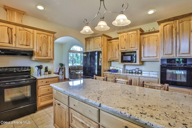 kitchen with black appliances, under cabinet range hood, light stone counters, arched walkways, and light tile patterned flooring