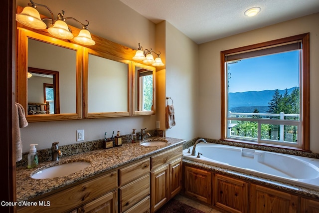 full bath with a garden tub, double vanity, a mountain view, and a sink