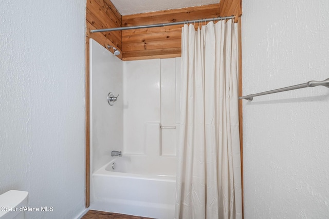 bathroom featuring shower / bath combination with curtain, toilet, and a textured wall