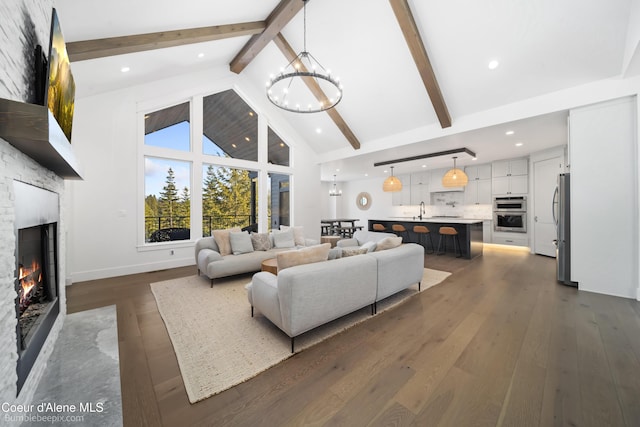 living area featuring high vaulted ceiling, a lit fireplace, a chandelier, dark wood finished floors, and beam ceiling