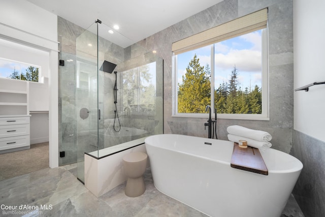 full bath featuring plenty of natural light, a tile shower, marble finish floor, and tile walls