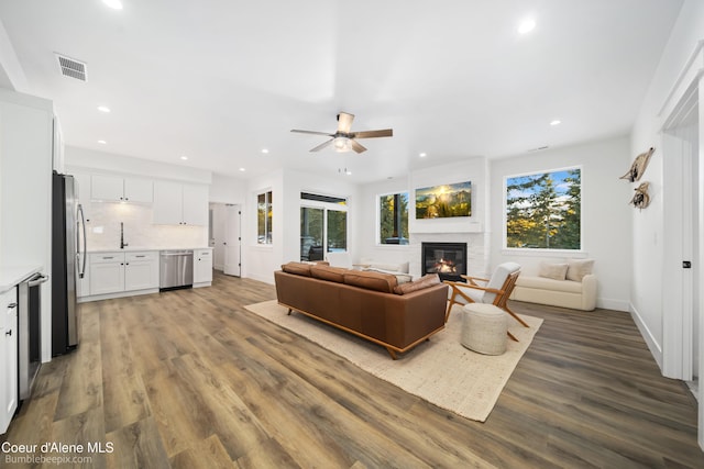 living area with a ceiling fan, wood finished floors, a glass covered fireplace, and visible vents