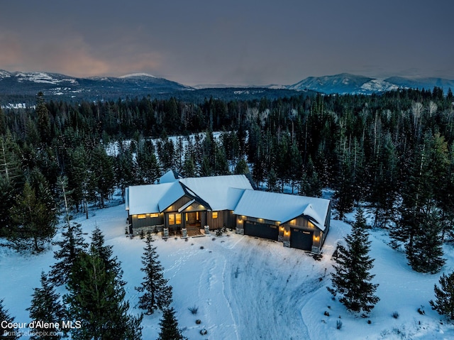 snowy aerial view featuring a forest view and a mountain view