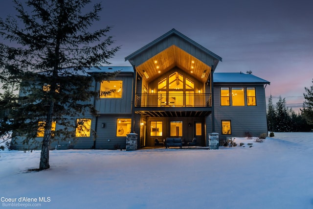 snow covered rear of property featuring a balcony and board and batten siding