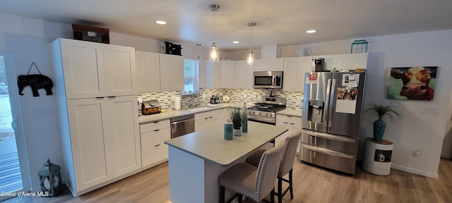 kitchen with backsplash, appliances with stainless steel finishes, light wood finished floors, a breakfast bar, and white cabinetry