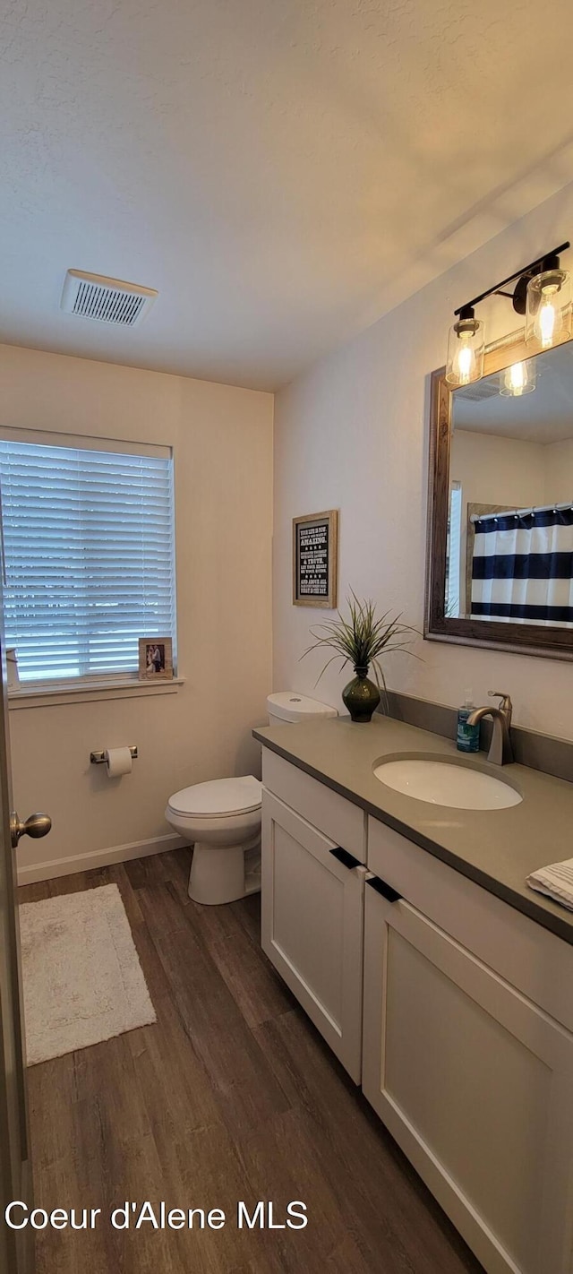 bathroom with visible vents, vanity, wood finished floors, toilet, and baseboards