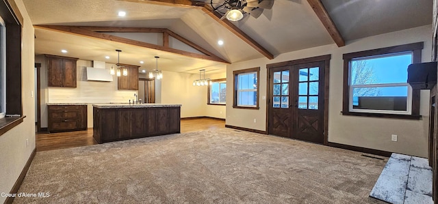 kitchen featuring ventilation hood, carpet floors, baseboards, vaulted ceiling with beams, and a center island with sink
