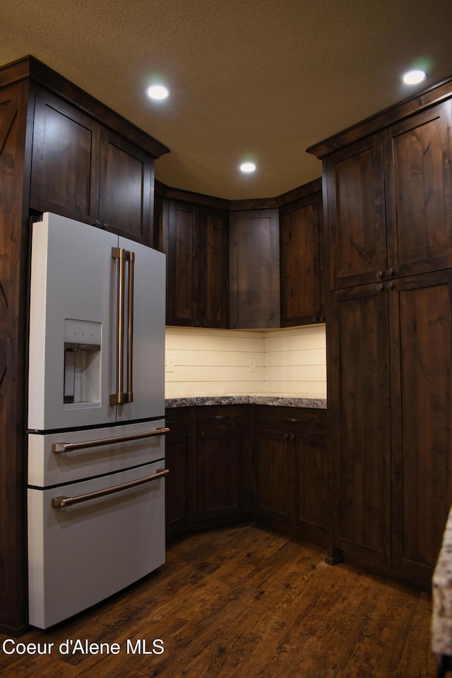 kitchen with high end white refrigerator, dark brown cabinetry, dark wood-style flooring, and a textured ceiling