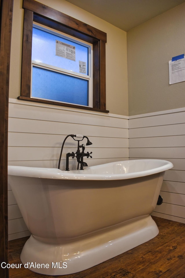 full bathroom featuring a soaking tub, wood walls, wood finished floors, and a wainscoted wall