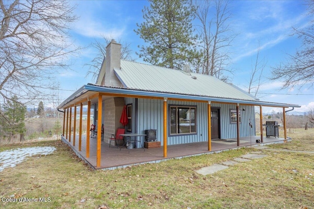 back of house with a lawn, metal roof, a chimney, and board and batten siding