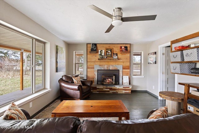 living room featuring hardwood / wood-style floors, a large fireplace, baseboards, and a ceiling fan