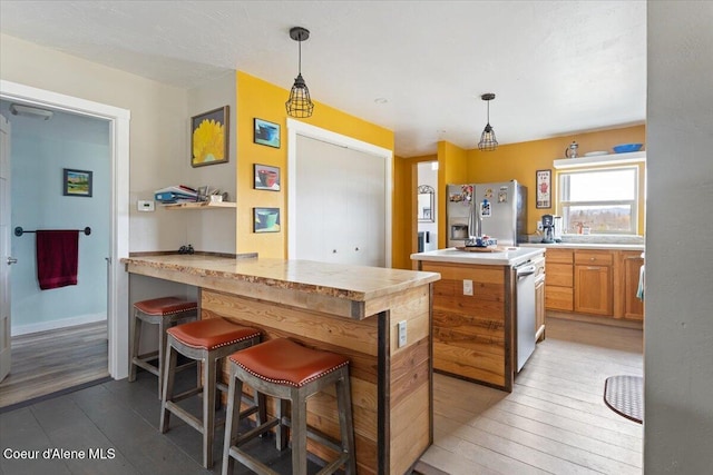 kitchen with light countertops, light wood-type flooring, stainless steel fridge with ice dispenser, pendant lighting, and a peninsula