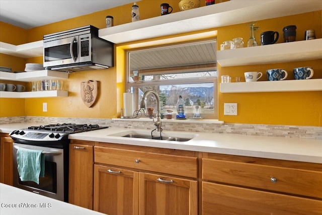 kitchen featuring light countertops, a sink, open shelves, brown cabinets, and stainless steel appliances
