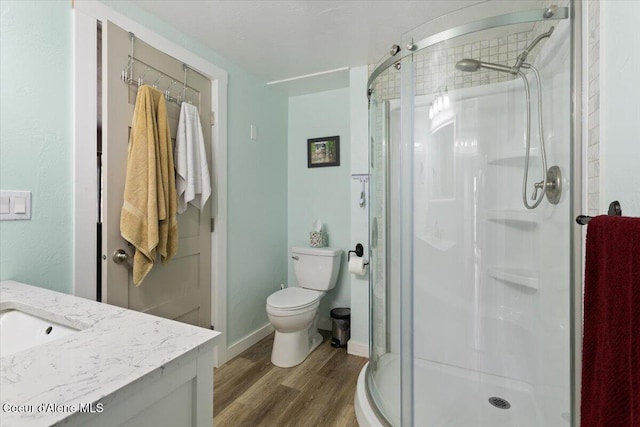 full bath with a shower stall, baseboards, wood finished floors, toilet, and vanity