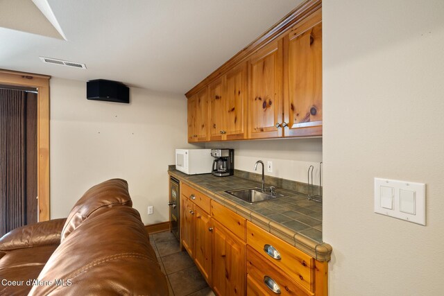4459 E Ogara Rd, Harrison, ID 83833 - kitchen featuring tile counters, a sink, visible vents, white microwave, and brown cabinetry