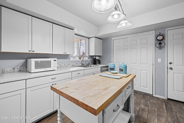 kitchen with a sink, white microwave, white cabinetry, dark wood finished floors, and a kitchen island
