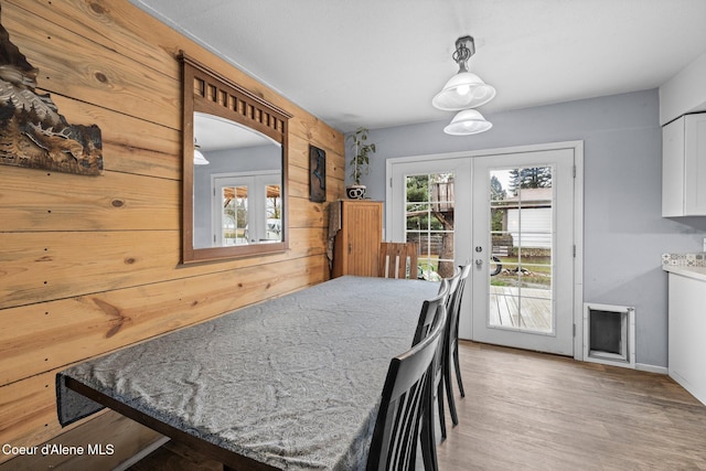 dining space with french doors, plenty of natural light, wooden walls, and light wood-style floors