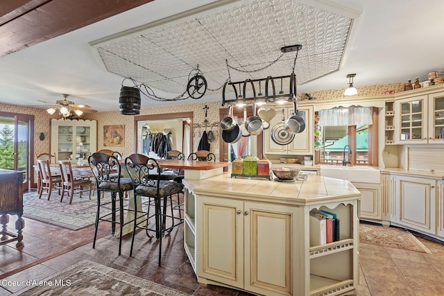 3467 E Sunset Dr, Harrison, ID 83833 - kitchen featuring cream cabinets, open shelves, wallpapered walls, tile countertops, and a ceiling fan