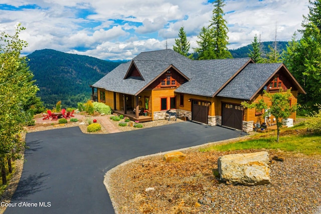view of front of house with covered porch, stone siding, aphalt driveway, a garage, and a mountain view