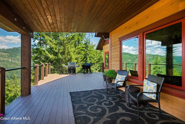 wooden terrace featuring area for grilling and a view of trees