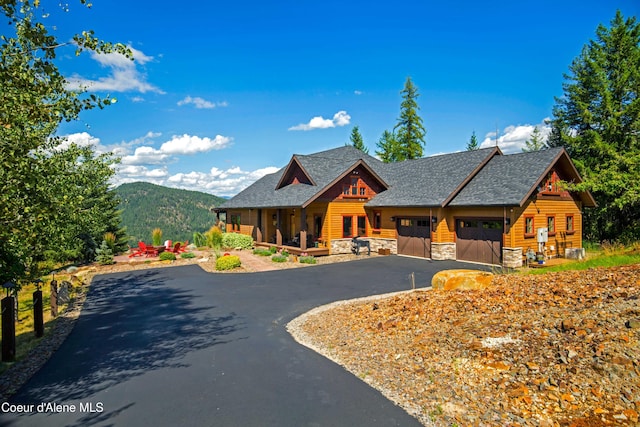 view of front facade with driveway, covered porch, stone siding, and a mountain view