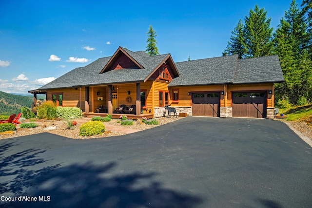 view of front of house featuring stone siding, roof with shingles, an attached garage, aphalt driveway, and a porch
