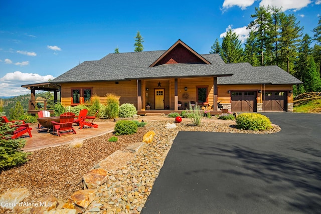 view of front of house with stone siding, aphalt driveway, a garage, roof with shingles, and covered porch