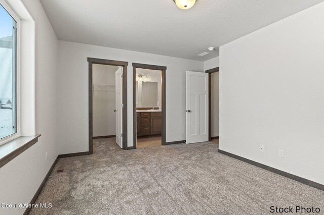 11669 N Railway Ave, Rathdrum, ID 83858 - unfurnished bedroom with light carpet, a walk in closet, baseboards, ensuite bath, and a closet