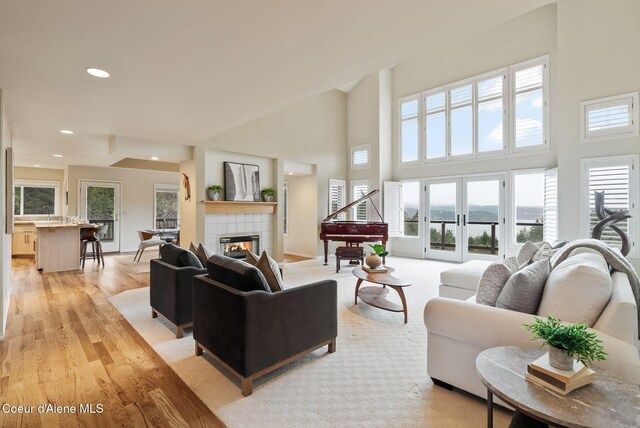 living room featuring a tiled fireplace, a high ceiling, light wood-type flooring, baseboards, and recessed lighting
