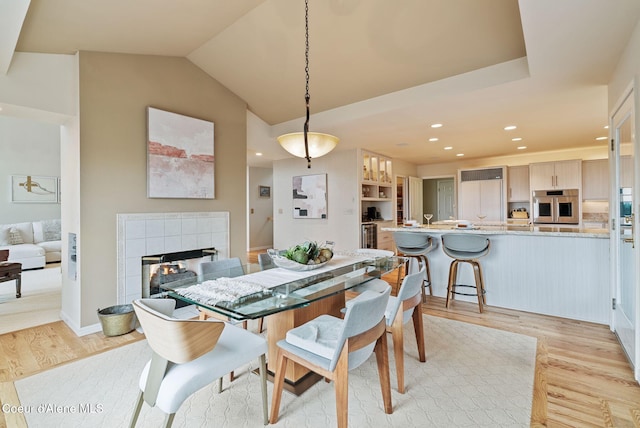 dining room with a tiled fireplace, recessed lighting, lofted ceiling, and light wood-type flooring