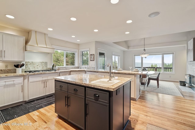 kitchen featuring stainless steel gas cooktop, a sink, a peninsula, custom exhaust hood, and a kitchen island with sink