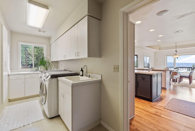 laundry area with independent washer and dryer, a sink, light wood finished floors, visible vents, and cabinet space