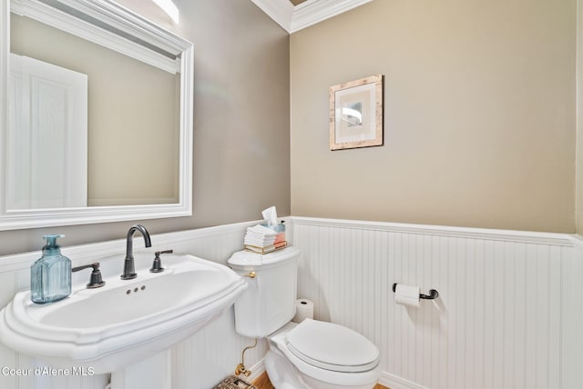 half bath featuring wainscoting, crown molding, toilet, and a sink