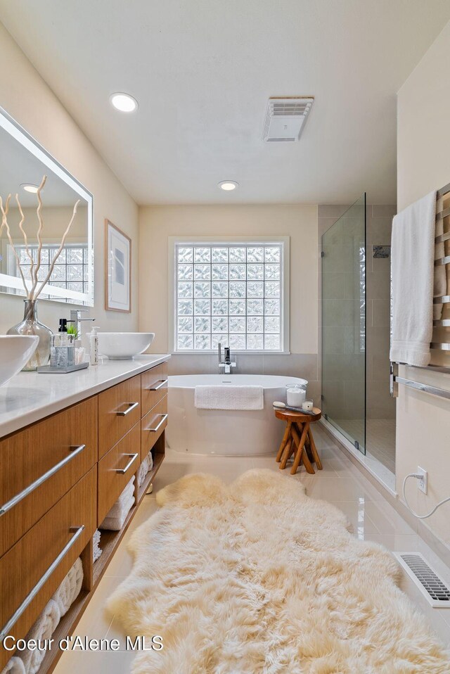 full bath featuring double vanity, visible vents, a stall shower, and a soaking tub