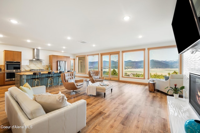 living room featuring recessed lighting, light wood-style floors, a glass covered fireplace, and a healthy amount of sunlight