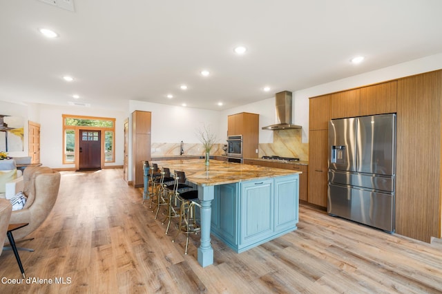 kitchen with wall chimney range hood, a kitchen breakfast bar, light wood-type flooring, and appliances with stainless steel finishes