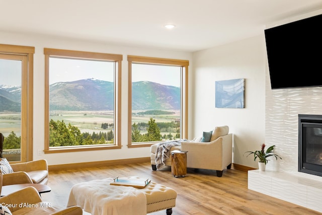 living area featuring a tile fireplace, baseboards, a healthy amount of sunlight, and wood finished floors
